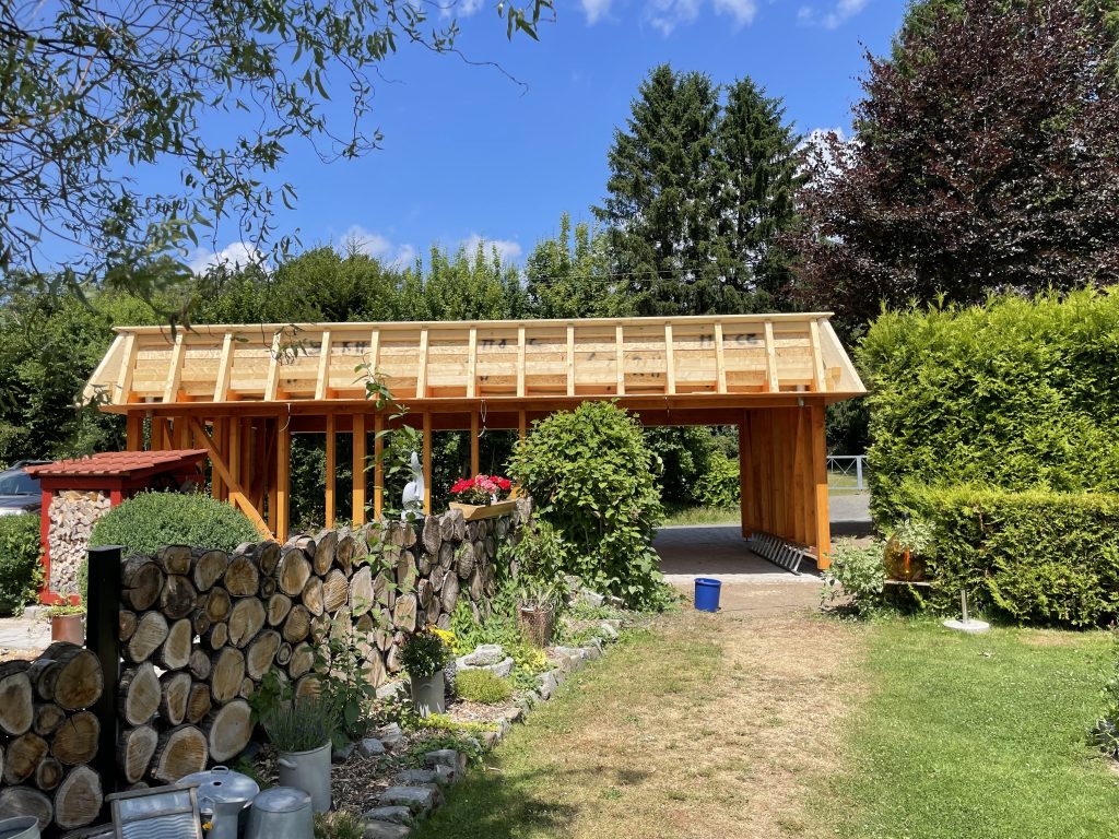 Holz-Carport mit umlaufender Attika in offener Gartenumgebung – Seitenansicht im Rohbau